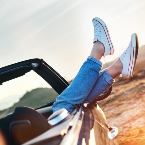The passenger in a convertible with their feet hanging over the side of the car, showcasing their sneakers.