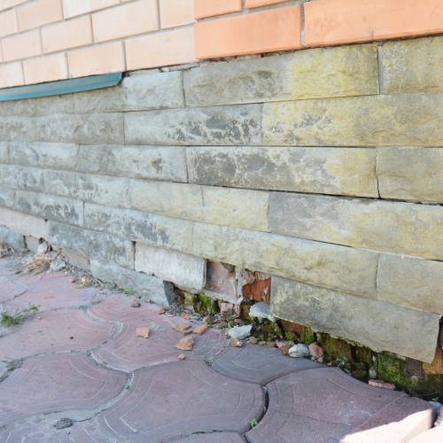 A home's exterior displaying cosmetic foundation damage with misplaced bricks, cracking, and uneven lines.