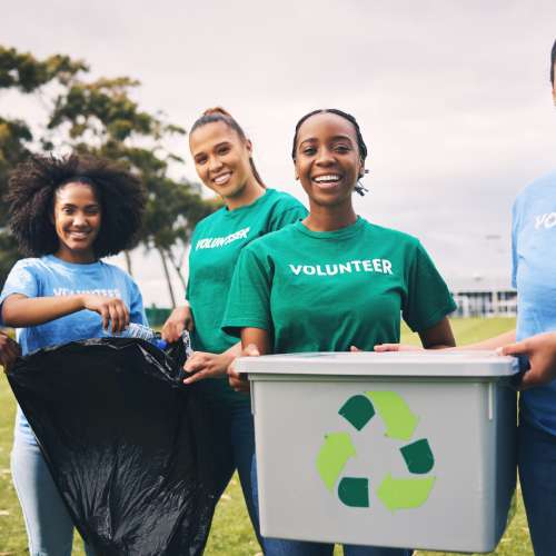 A group of five female volunteers smile as they collect litter and recyclables during a community clean up project.