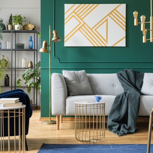 A gray sofa sits in front of a green accent wall decorated with a large gold and white canvas with geometric shapes.