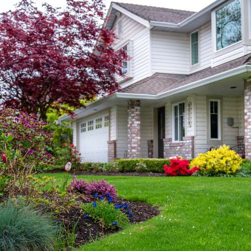 A beautiful house in a residential neighborhood with a nice landscaped yard with colorful blooming flowers and shrubs.