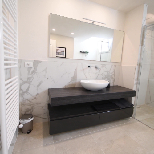 A spacious, modern bathroom contains a black vanity, white sink, grey and white tile, and a walk-in shower.