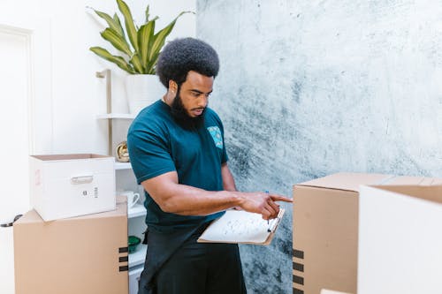 Free Mover checking inventory list while organizing cardboard boxes in a new apartment. Stock Photo