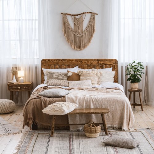 A cozy, warm bedroom with white linens, wooden accents, and rustic design features. There's a plant in the corner.