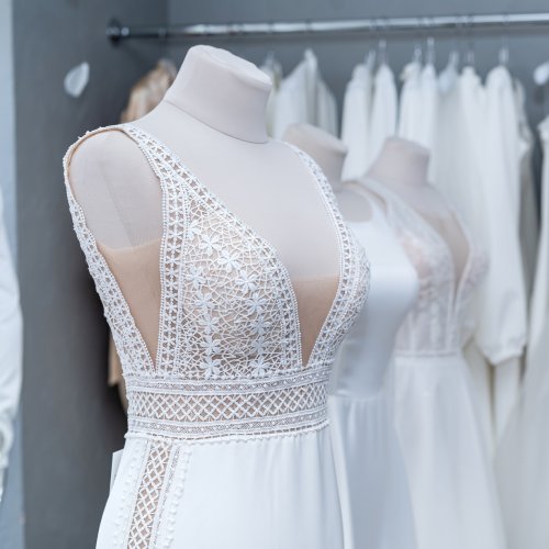 A mannequin is fitted with an elegant white wedding gown placed in front of a rack full of dresses in the background.