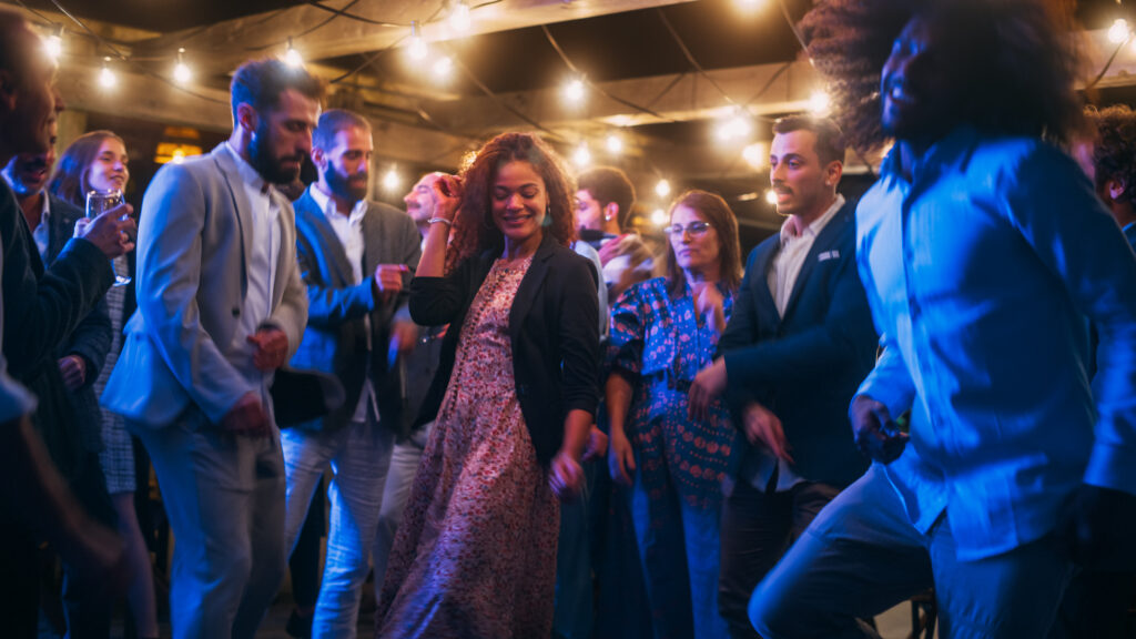 A large group of young adults dancing together at a wedding. They're all dressed nicely and having fun.