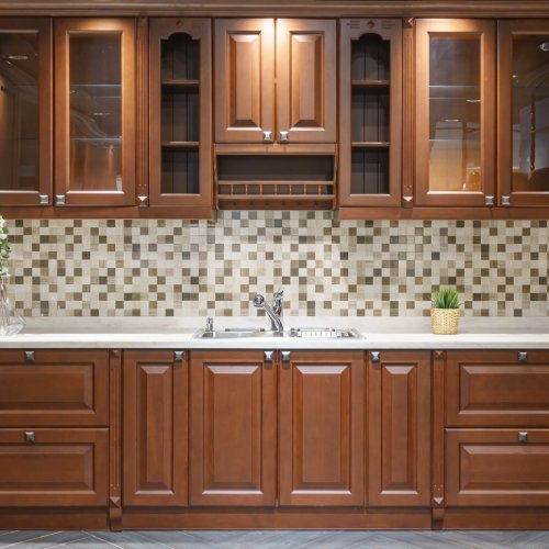 A kitchen interior with red-brown cabinet stain and marble countertops. The backsplash is gray and white check.