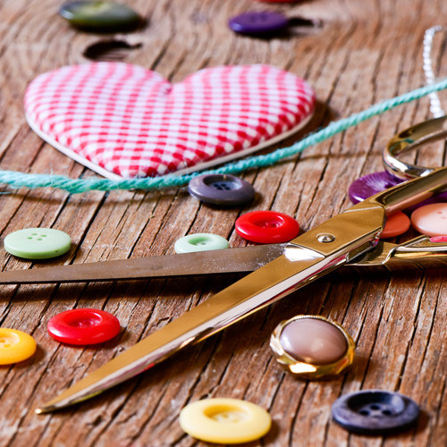 A wooden table with a collection of sewing notions, including buttons, scissors, yarn, and a heart-shaped pin cushion.