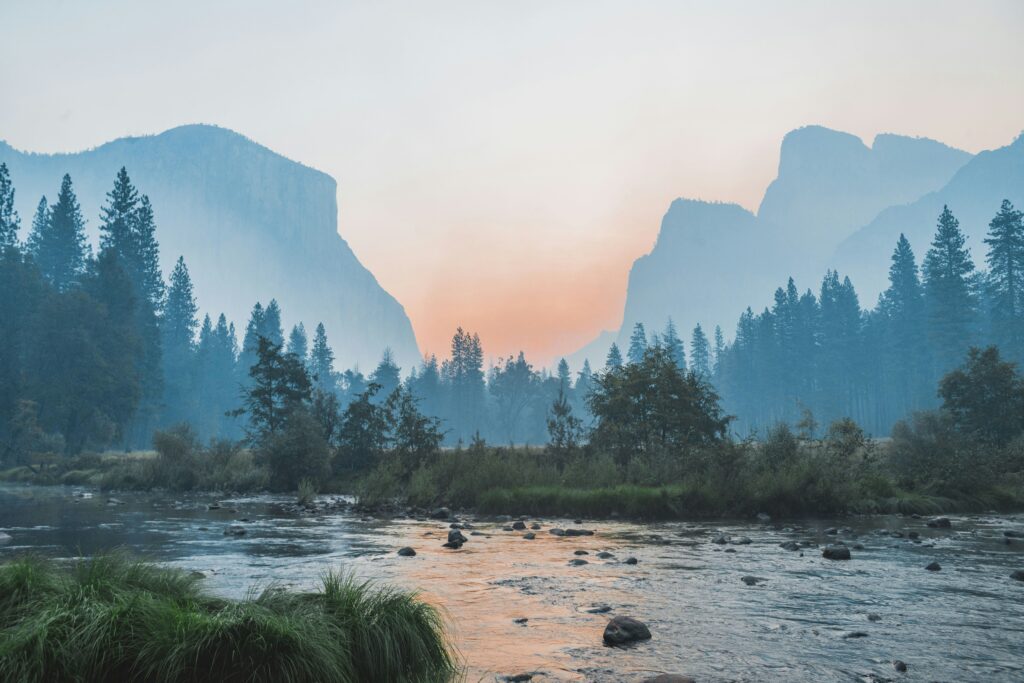 Scenic sunrise in Yosemite Valley with river, misty mountains, pine trees, and granite cliffs