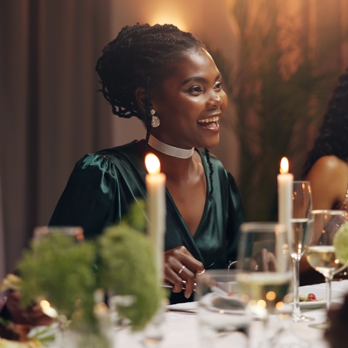 Three women dressed elegantly, enjoying a candlelit dinner, smiling and talking around a table with wine glasses.