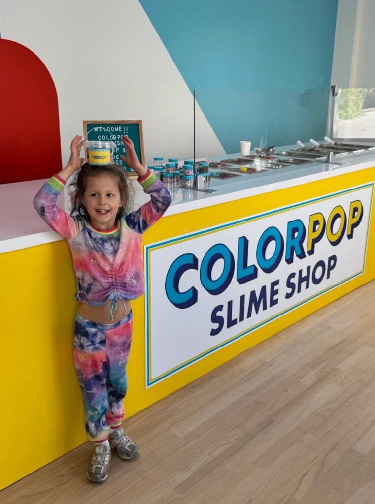 Young girl standing in front of the colorful ColorPop Slime Shop counter in Southampton.