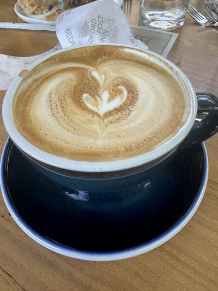 Latte with heart-shaped latte art in a dark blue ceramic cup at Bedford Post Inn, served on a wooden table during brunch in Bedford, New York.