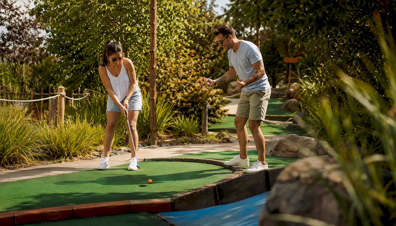 Couple playing mini-golf outdoors in sunlight