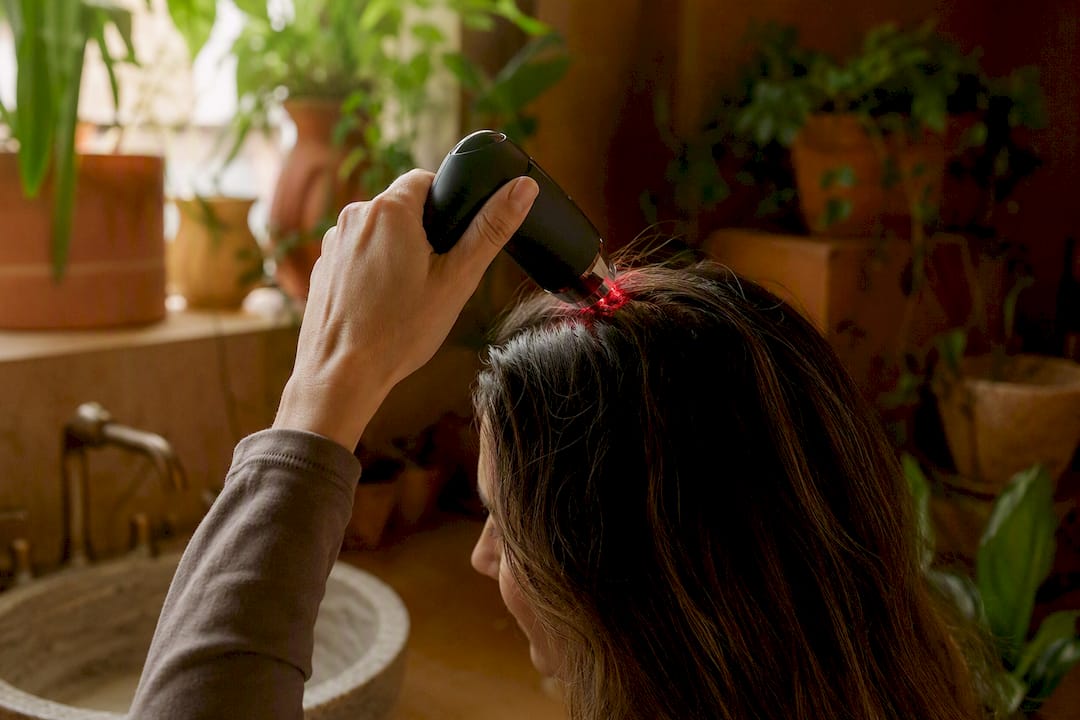 Applying red light therapy wand to scalp