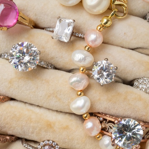 Assorted diamond, pearl, and gemstone rings and earrings arranged in rows on a cream velvet jewelry tray.