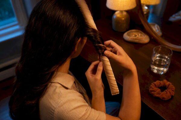 Hands wrapping damp hair around satin rod