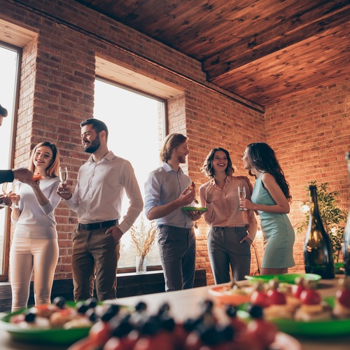 A group of employees gathering to socialize during a company-wide celebration. There's a table with refreshments.